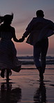 Sunset, couple and holding hands in ocean for running, love and travel adventure for summer holiday. Back, evening or people outdoor at beach with relationship, romantic getaway or happy on vacation.