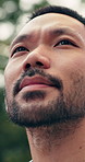 Thinking, calm and Asian man in park with sightseeing, mindfulness and fresh air on summer break. Low angle, bokeh and person with breathing, reflection and peaceful perspective on outdoor trip.