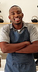 Face, black man and waiter with arms crossed in cafe, entrepreneur and about us for hospitality. Portrait, male person and server at coffee shop with smile, positive attitude and catering industry
