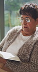 Bible, learning and religion with old woman in living room for Christian belief or spiritual study. Book, faith and reading with senior person on chair in retirement home for gospel, hope or trust