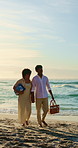 Couple, holding hands and smile with picnic basket at beach, bonding and summer holiday with partner. Outdoor, happy people and walk with spouse on coastal vacation, space and commitment in nature