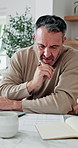 Man, laptop and documents in home for finance, budget planning or asset management in kitchen. Mature person, typing or checking invoices with tech for financial expenses and paperwork in house