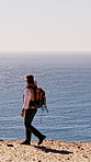 Walking, hiking and man with ocean view on journey, adventure or trip for exploration on vacation. Trekking, holiday or person outdoor by cliff for tourism, travel  or sightseeing with scenery of sea