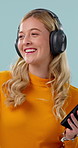 Phone, headphones and happy woman in studio with dance, internet and listen to popular music playlist. Person, smile and audio tech with streaming app, radio and rhythm for song on blue background.