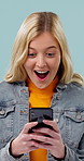 Happy, woman and surprise in studio with phone, text message notification or alert for giveaway win. Person, shock and smile with tech, social media announcement or winner of prize on blue background