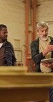 Carpenter, tablet and collaboration for planning, manufacturing or supervisor guidance. Woodwork, men and talking with tech for training, point or walk with team for production inspection in workshop