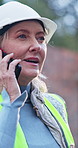 Engineer, talk and phone call at construction site with rain, safety update or concern for building. Mature woman, feedback and tech outdoor with contact, winter or advice for engineering operations.