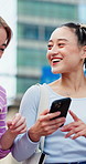 Women, friends and walk in city with phone, conversation and laugh for funny gossip on weekend break. Happy, Japanese people and talk outdoor in urban town with tech, social media meme and bonding.
