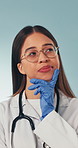 Thinking, woman and doctor in studio with planning, decision or problem solving for medical career. Glasses, gloves and healthcare worker on blue background with solution, idea or choice on service.