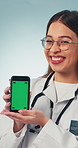 Face, phone and doctor with green screen in studio for medical news, telehealth app or advertising. Healthcare, portrait and happy woman with cellphone, mockup space or clinic info on blue background