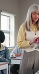 Woman, teacher and walking in classroom with paper, assignment and school quiz for education. Person, teaching and students at campus with documents, exam revision and assessment results for learning