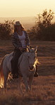 Sunset, woman and cowgirl horse riding on farm with hat, companion or bonding together on adventure. Calm, person and travel outdoor in countryside with stallion, peaceful journey or animal in Texas.
