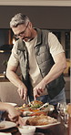 Thanksgiving, man and cutting chicken in family home with conversation, lunch feast and healthy food. Mature person, serving meal and gathering in dining room with tradition, discussion or nutrition.