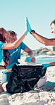 Volunteer, team and cleaning at beach with high five, plastic bag and recycling goals for non profit. Happy, people and pick up trash outdoor by ocean with support, conservation and sustainable NGO.