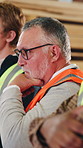Man, carpenter and thinking with team in seminar workshop for timber production or lumber logistics. Mature, male person or artisan listening in warehouse for speech or presentation in warehouse