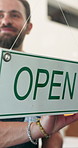 Smile, man and open at cafe with sign, start day and storefront invitation for hospitality service. Happy, business owner and signage at coffee shop for welcome, trading hours and availability notice