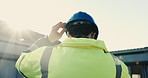 Electrician, helmet and man at construction site with inspection, safety or property development job. Back, flare and person outdoor by building with PPE, project and technician for electrical work.