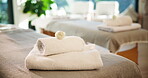 Towels, spa and bed for massage at resort, wellness retreat and flower decoration with body care. Complimentary gift, luxury or holistic therapy with cloth stack, lodge or hotel with cosmetic service