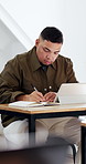 Student, writing and learning in university with tablet, notebook and watch video for test revision. Man, study and taking notes in college classroom with tech, knowledge and tutorial for education.