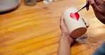 Artisan, painting and hands with cup in&nbsp;workshop, creative and drawing heart shape with paintbrush. Pottery, craftsmanship and person with handmade mug, above and art process with equipment or color