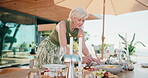 Home, food and host outdoor for table setup with charcuterie board, snacks and prepare for event. Mature woman, healthy diet and happy on patio for gathering, party or catering in house backyard
