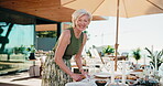 Face, food and host for home table setup with smile, snacks and prepare lunch for social event. Mature woman, healthy diet and happy on patio for gathering, party or catering in house backyard
