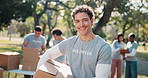 Man, volunteer and face in park with box, campaign and happy for community outreach program. NGO, humanitarian and team in nature for food drive, social responsibility or donation project for charity