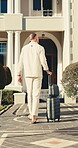 Travel, man and walking with luggage for hotel arrival, weekend stay and getaway destination. Back, guest and suitcase outdoor for solo trip, accommodation entrance and check in for vacation booking