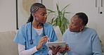 Nurse, tablet and discussion in retirement home with old woman, explain test results and diagnosis. Black people, healthcare worker and senior patient talk on sofa with tech, medical advice and help.
