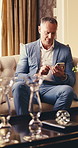 Phone, business and man in hotel lounge for digital check in, luxury hospitality or scroll email. Mobile, mature person and worker in accommodation for travel, deluxe resort and communication app