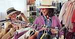 Fashion, shopping and woman with friends for fitting, retail therapy or excited with choice at store. Happy people, boutique and try clothes with stylish hat at rack, talk and wow for customer deal