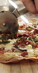 Person, hands and cutter with pizza on board for fast food, dining recipe or meal prep in home. Pastry chef, cutting and slice with ingredients, dairy snack or cuisine for baked dinner in house