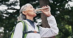 Hiking, break and old woman drinking water in nature with adventure, thinking or retirement wellness. Bokeh, senior person and reflection outdoor in forest with trekking, hydration and low angle.