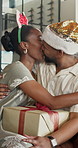 Christmas, kiss and couple with present, home and bonding with partner on December holiday and love. Xmas, connection and black people with gift for festive season, happy and embrace in living room